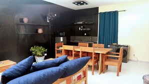Un espacio habitable compacto con kitchenette, un comedor con mobiliario de madera y un sofá azul.