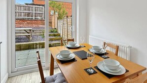 A dining area with a wooden table set for four, a sliding glass door leading to an outdoor patio, and a white radiator on the wall. - 2bedroom sleeps 6 garden driveway Free Gym Access (Grantham)