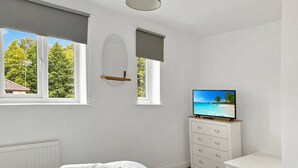 A bedroom with a bed, two rolled towels, a TV, a dresser, and a window with a view of trees. - 2bedroom sleeps 6 garden driveway Free Gym Access (Grantham)