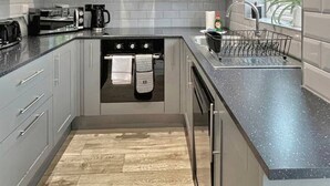 A modern kitchen with grey cabinets, a black stove, and a window with a view. - 2bedroom sleeps 6 garden driveway Free Gym Access (Grantham)