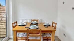 A dining area with a wooden table set for four, white chairs, and a view of the outside through a glass door. - 2bedroom sleeps 6 garden driveway Free Gym Access (Grantham)