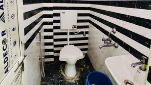 A small, narrow bathroom with a toilet, sink, and blue buckets. - Hotel City Moon (Ujjain)
