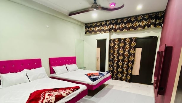 A hotel room with two beds, a ceiling fan, and a door with a patterned curtain. - Hotel City Moon (Ujjain)