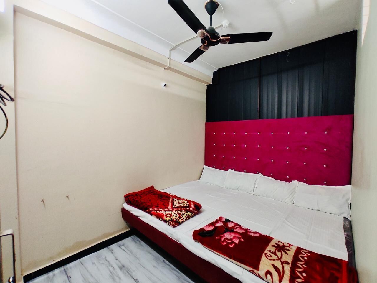 A small bedroom with a bed, a ceiling fan, and a red and black headboard.
