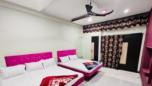 A room with two beds, each with a pink headboard and white bedding. There is a ceiling fan and a door with a floral curtain. - Hotel City Moon (Ujjain)