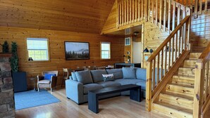 A cozy cabin interior with a wooden staircase, a gray sofa, and a dining area. - Spectacular Mountain Views. Peaceful Solitude. Rustic cabin with modern comforts. 90 mins from DC (Rileyville)