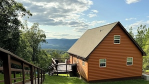 A wooden cabin with a deck, surrounded by lush greenery and mountains in the background. - Spectacular Mountain Views. Peaceful Solitude. Rustic cabin with modern comforts. 90 mins from DC (Rileyville)