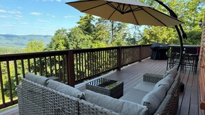 A deck with wicker furniture and a table, overlooking a scenic landscape. - Million Dollar Views. Peaceful Solitude. Rustic cabin.  90 minutes from DC. (Rileyville)