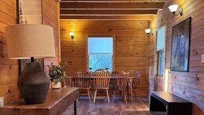 A wooden interior with a dining table, chairs, a lamp, and a window. - Million Dollar Views. Peaceful Solitude. Rustic cabin.  90 minutes from DC. (Rileyville)