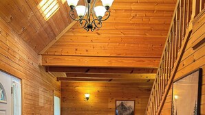 A cozy log cabin interior with a wooden ceiling, a chandelier, a sofa, a table with a lamp, and a painting on the wall. - Million Dollar Views. Peaceful Solitude. Rustic cabin.  90 minutes from DC. (Rileyville)