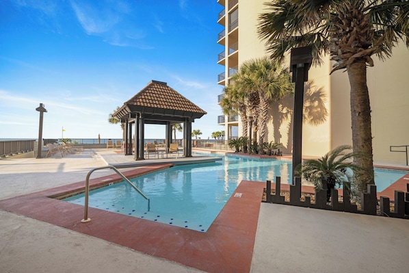 A swimming pool with a gazebo, palm trees, and a building with balconies.