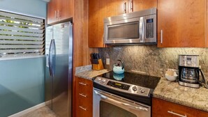A kitchen with stainless steel appliances, wooden cabinets, a granite countertop, and a kettle. - Royal Mauian, #207 2 Bedroom Condo (Kihei)