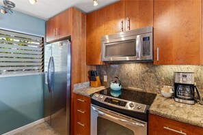 A kitchen with stainless steel appliances, wooden cabinets, a granite countertop, and a kettle. - Royal Mauian, #207 2 Bedroom Condo (Kihei)