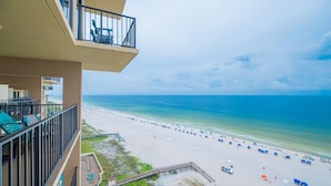 Blick auf einen Strand vom Balkon aus, mit blauem Himmel, sandigem Strand und einigen Sonnenschirmen.