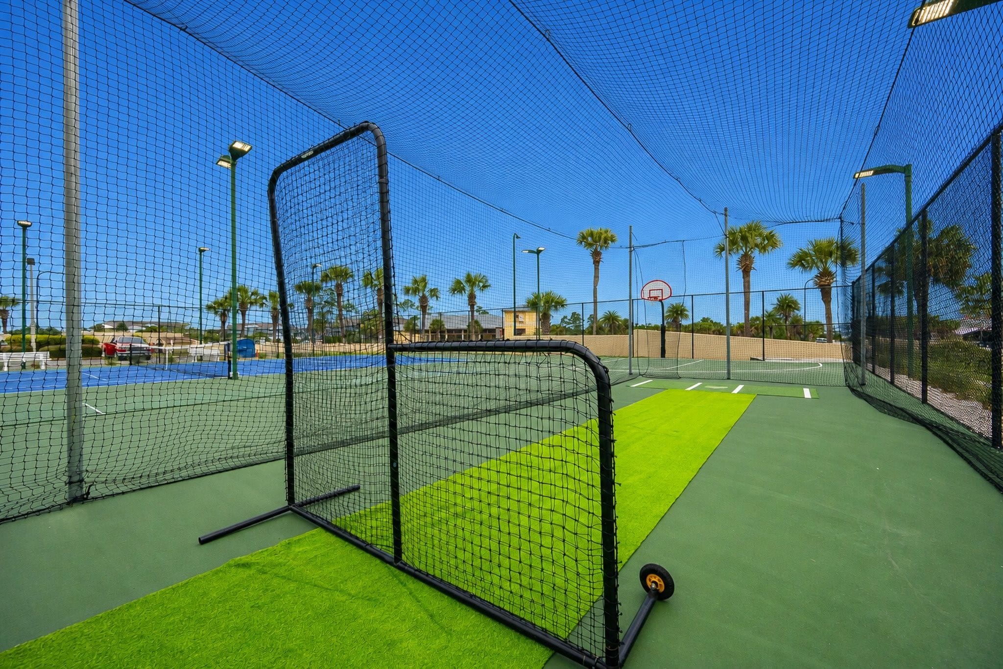 Cancha de tenis con red, césped sintético verde y aro de baloncesto.