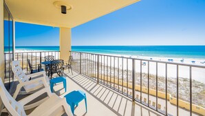 A balcony with a view of the beach, white lounge chairs, a table, and a blue stool. - Phoenix Ii 2045 2 Bedroom Condo (Orange Beach)