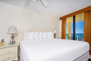 A hotel room with a bed, two bedside tables with lamps, a small decorative item, and a balcony with outdoor furniture. - Phoenix Ii 2045 2 Bedroom Condo (Orange Beach)
