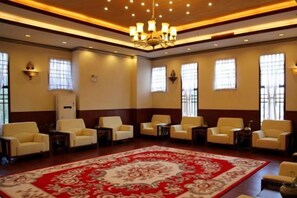Un hall d’hôtel doté d’une grande moquette rouge, de plusieurs espaces aménagés avec des sièges et d’un lustre.