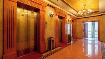 A hotel lobby with a polished floor, wooden elevator doors, and a chandelier.