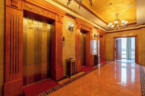 Un hall d’hôtel avec un sol ciré, des portes d’ascenseur en bois et un lustre.