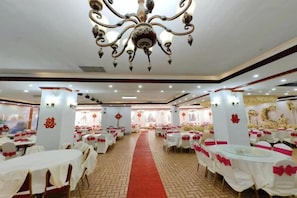 Une salle de banquet avec des tables rondes, une moquette rouge et des éléments décoratifs sur les murs.