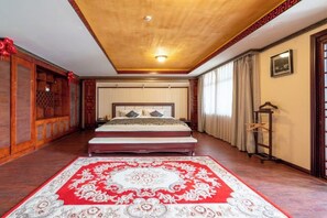 Ein Schlafzimmer mit einem großen Bett, Holzbalkendecke, Teppich mit roten und weißen Mustern und einem Kleiderschrank.