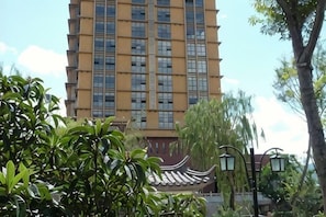 A tall building with a traditional architectural style, surrounded by greenery and street lamps.