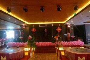 Une salle de banquet avec des tables rondes, une scène et des décorations traditionnelles.
