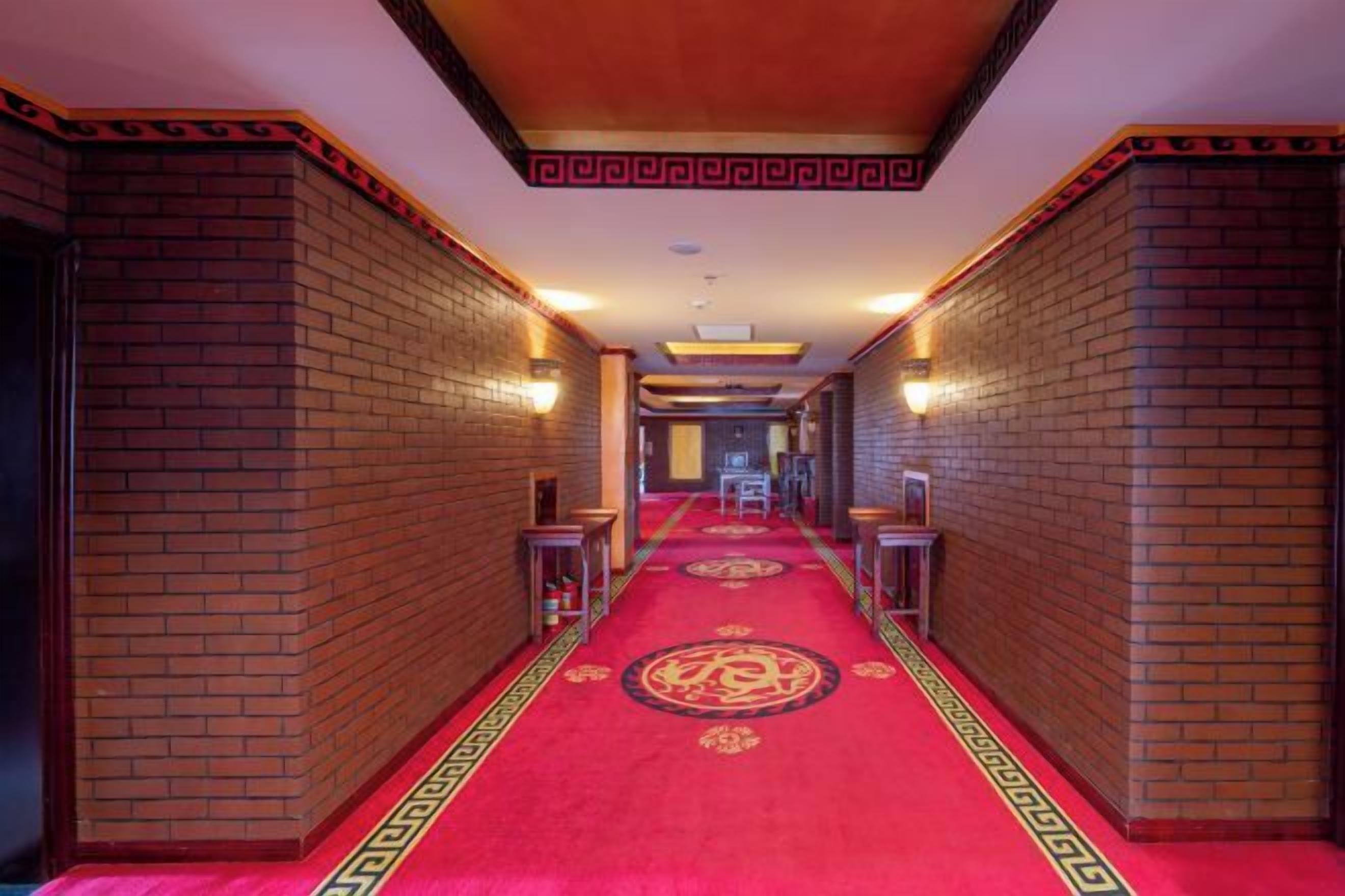 A hotel corridor with a red carpet, brick walls, and a patterned carpet runner.