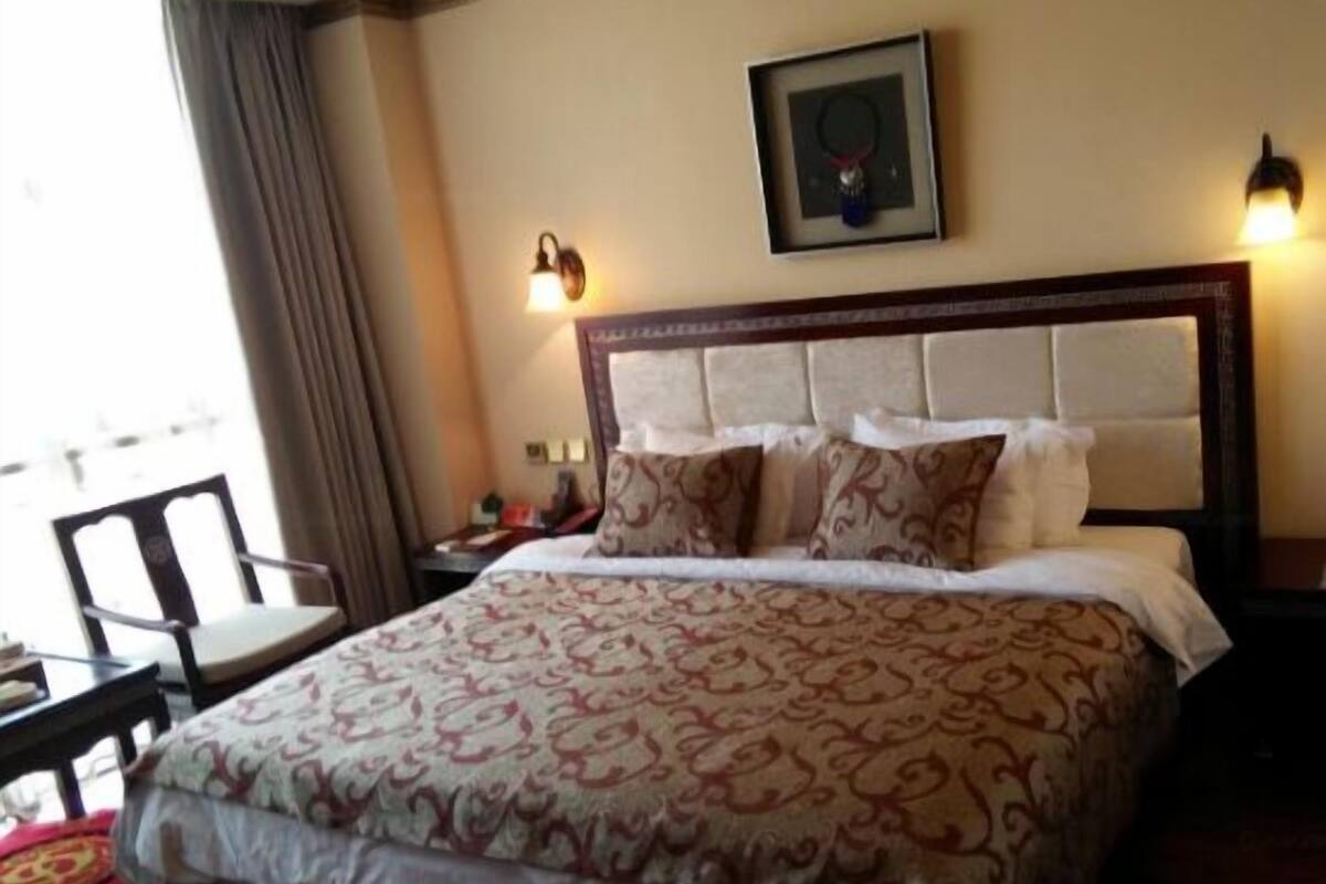 Hotelkamer met een bed, nachtkastje, stoel, lijst met foto aan de muur en raam met gordijnen.