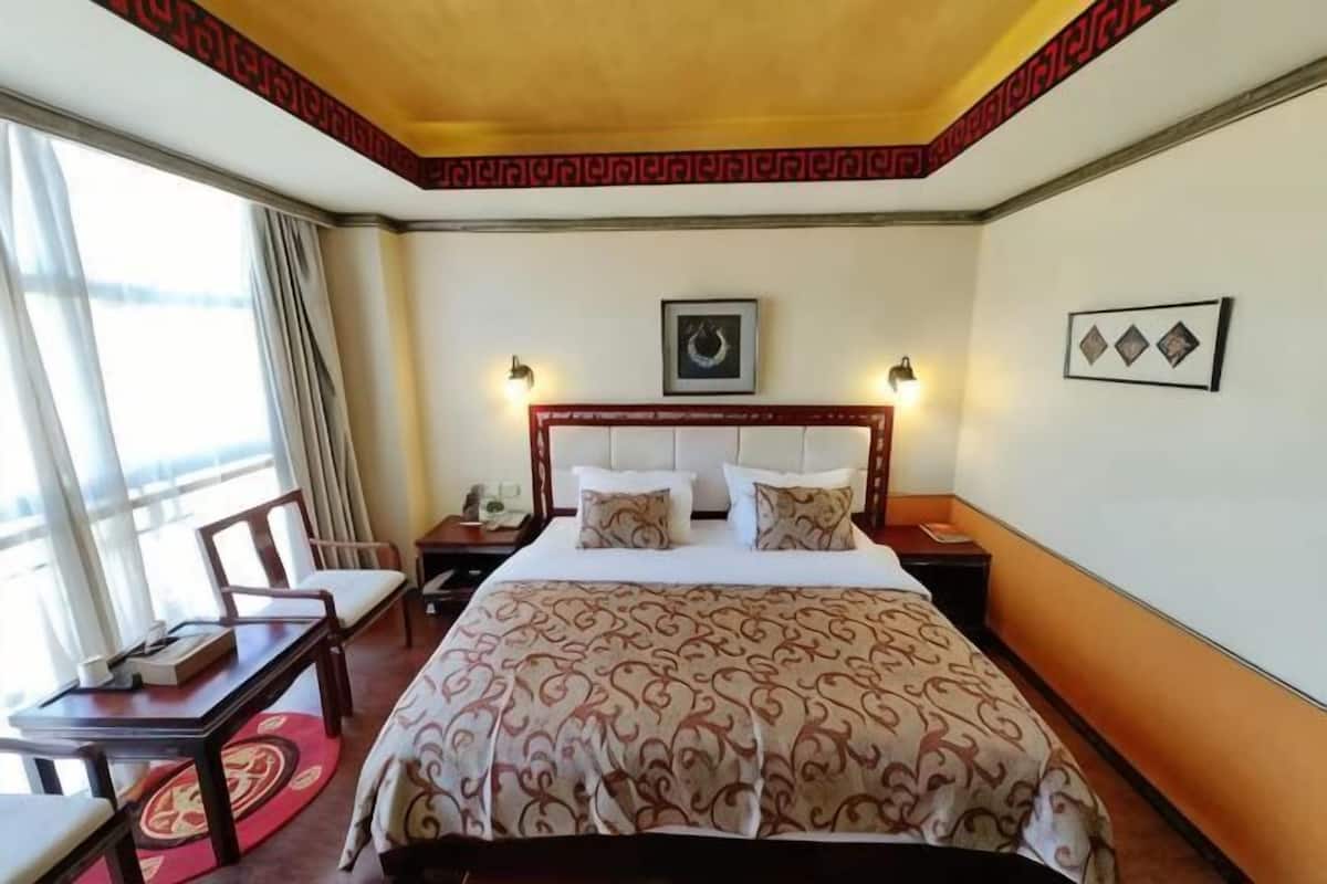 Een hotelkamer met een groot bed, een bureau met stoel, een nachtkastje en een raam met gordijnen.