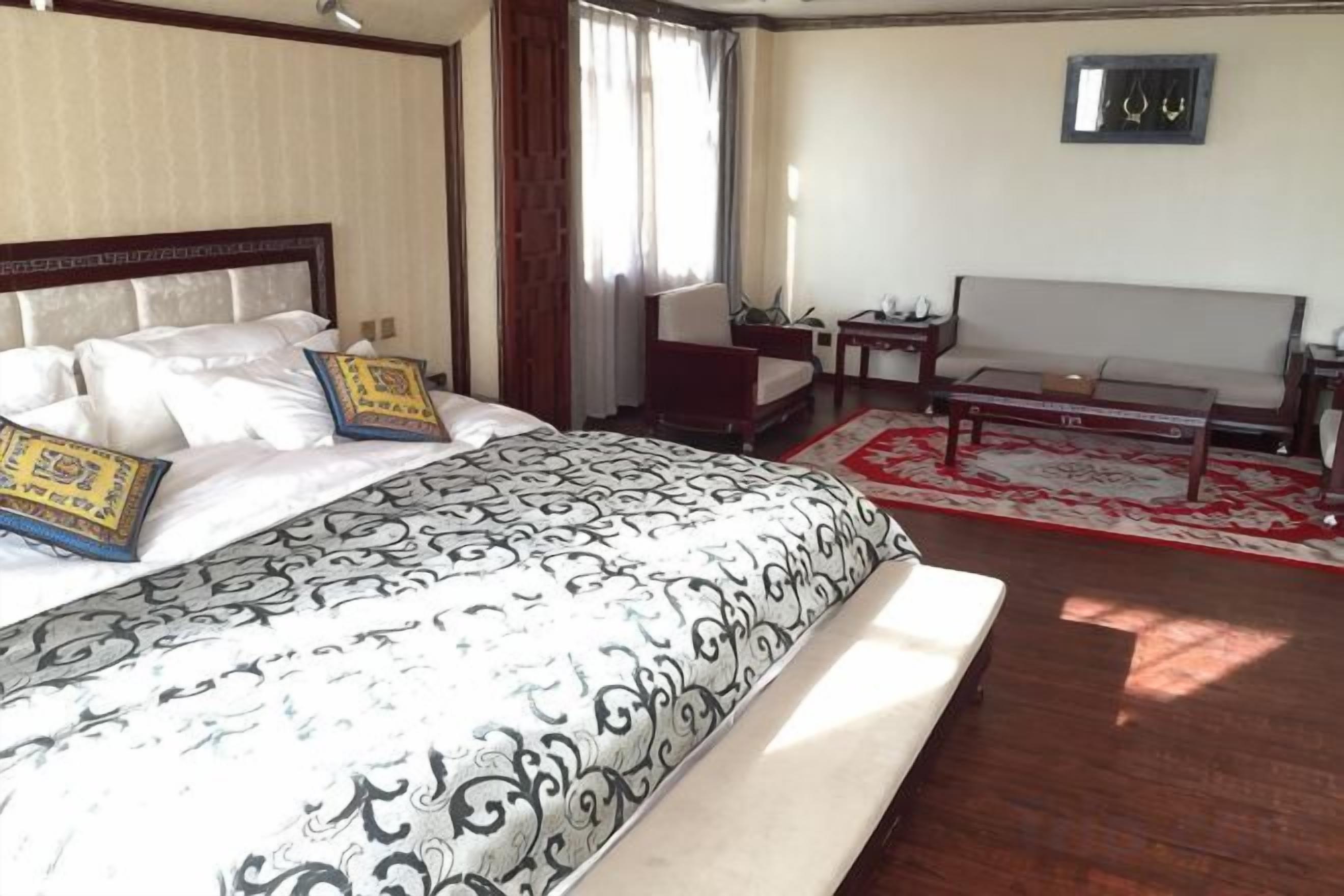 A hotel room with a large bed, a sofa, a small table, and a window with curtains.