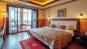 A hotel room with a large bed, a wooden floor, a red and gold patterned rug, a ceiling with a decorative pattern, and a window with a view of the outside. - Yijia Hotel (Wuding)