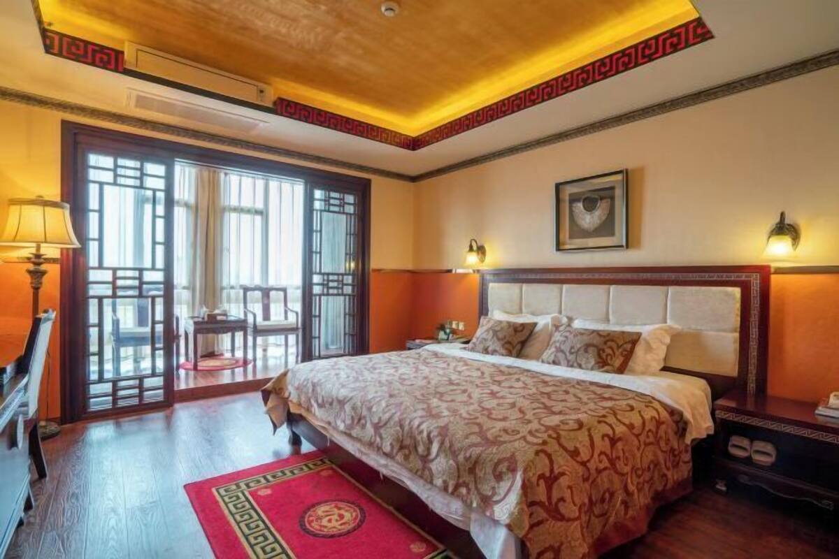 Hotelkamer met een groot bed, een houten vloer, een tapijt met een rood en gouden patroon, een plafond met decoratieve details en een raam met uitzicht.