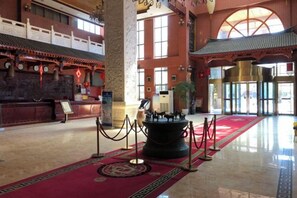 Un hall d’entrée avec un tapis rouge, un comptoir d’accueil et une grande colonne.