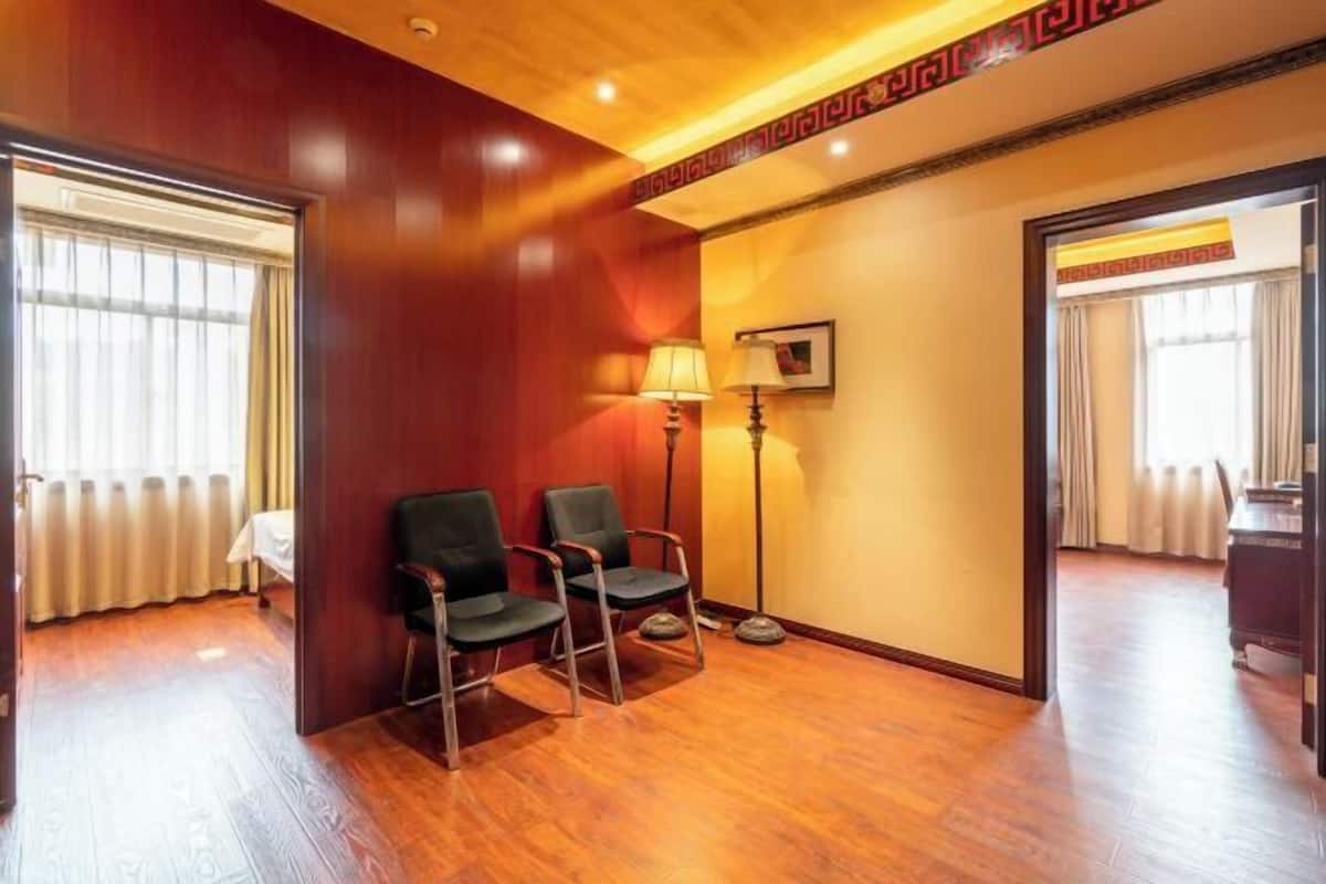 Een hotelkamer met houten vloer, twee zwarte stoelen, een vloerlamp en een bed met witte lakens.
