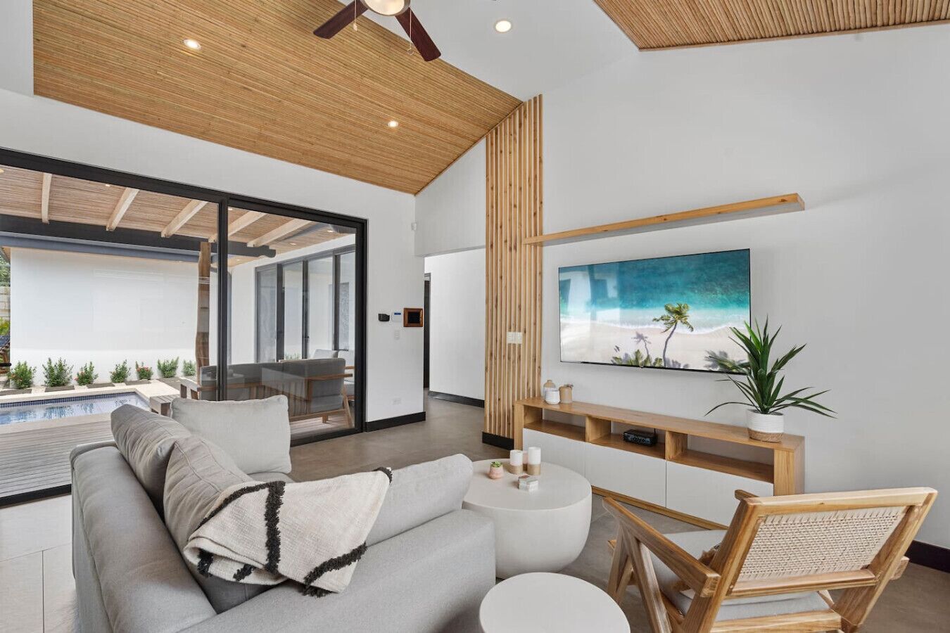 Un salon moderne avec vue sur la piscine, un téléviseur à écran plat et un plafond en bois.