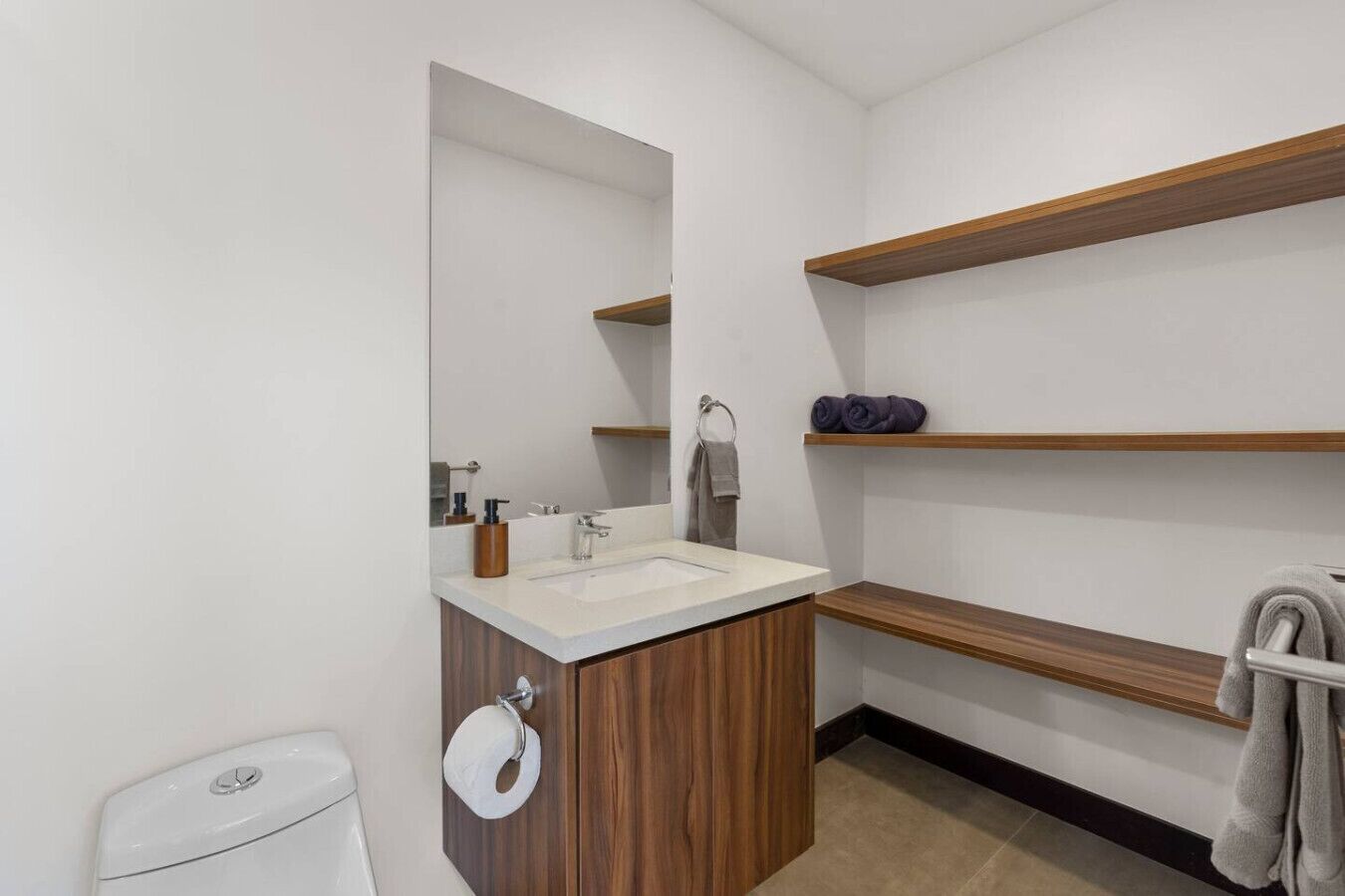A modern bathroom with a wooden vanity, a large mirror, a white sink, and built-in shelves.