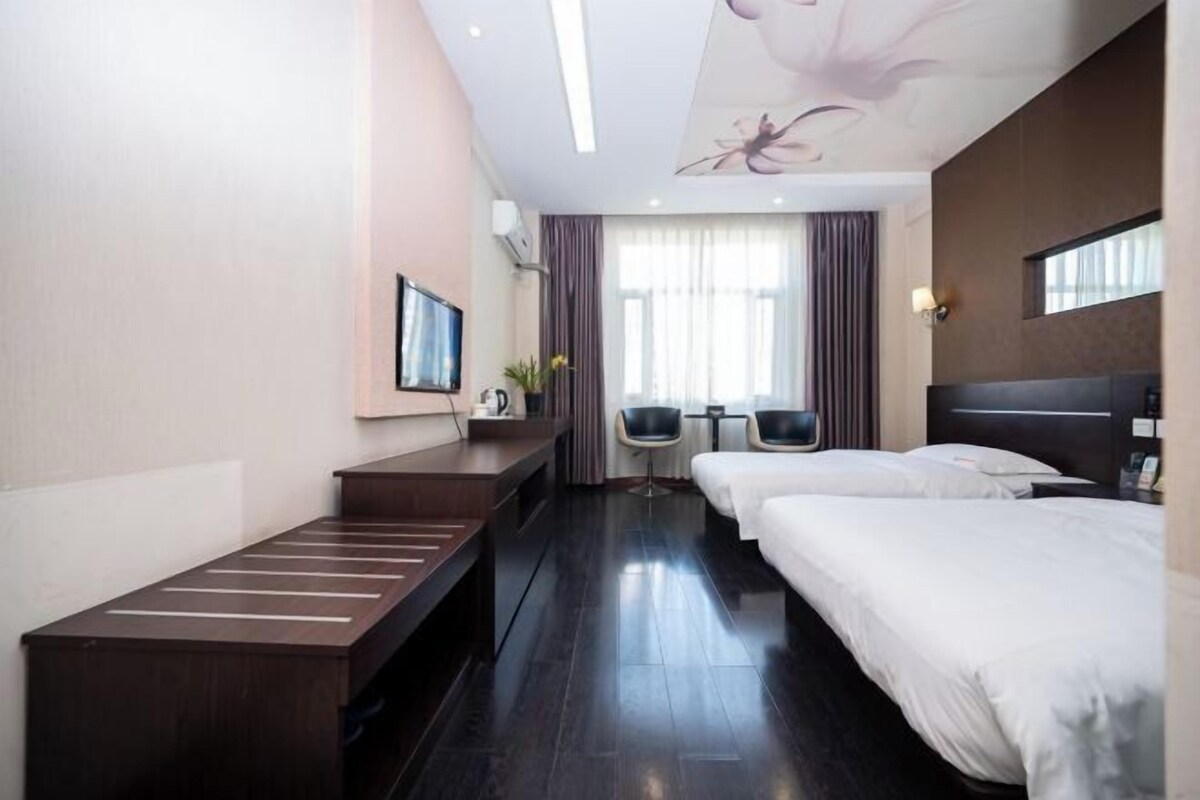 A hotel room with two beds, a desk, a chair, and a TV.