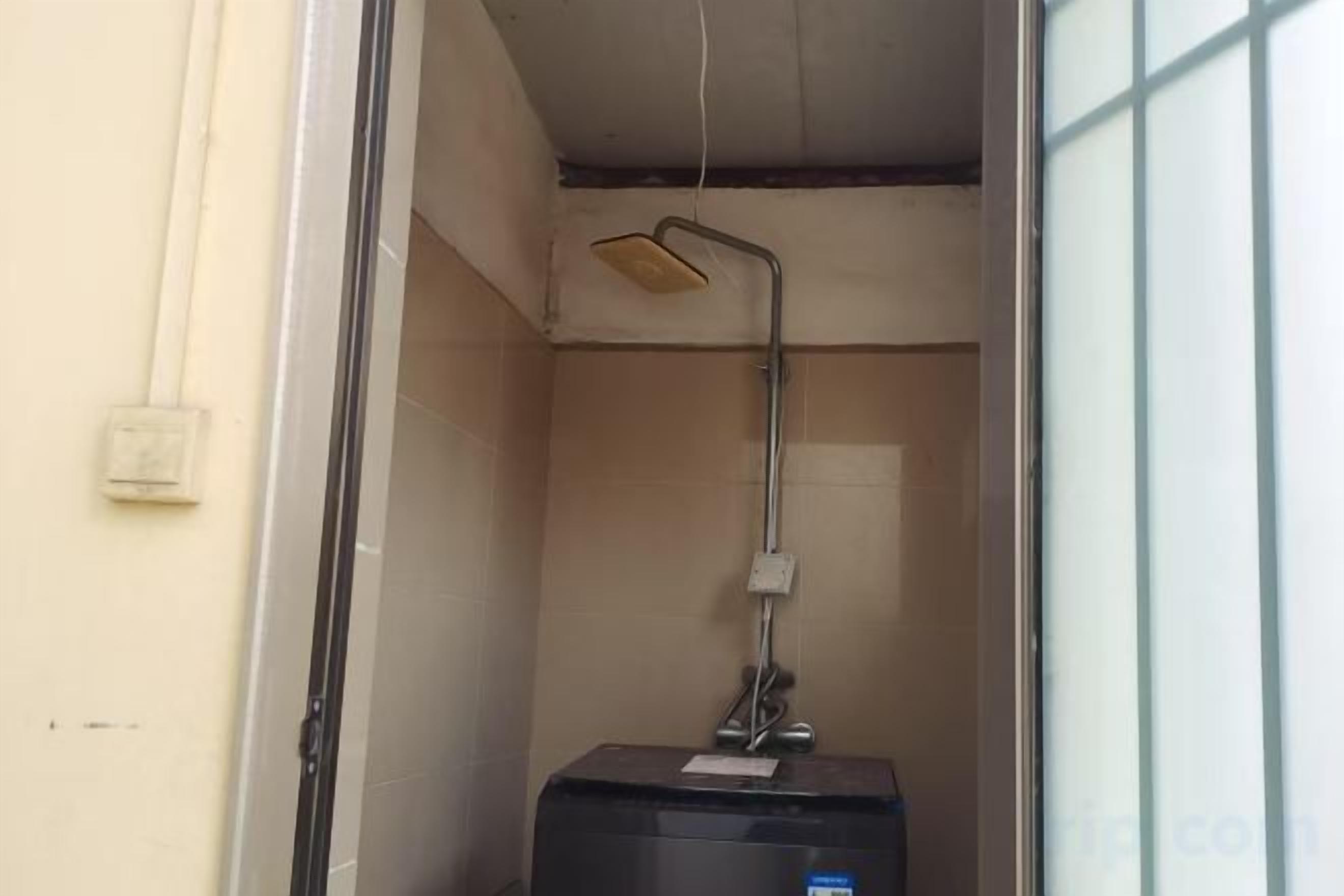 A small, enclosed bathroom with a shower, a visible electrical outlet, and a window.