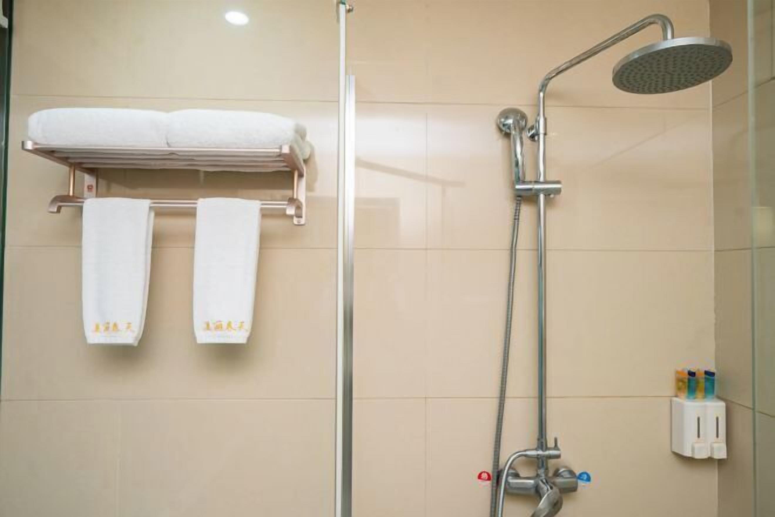 A bathroom with a shower, two towels hanging on a rack, and a soap dispenser on the wall.