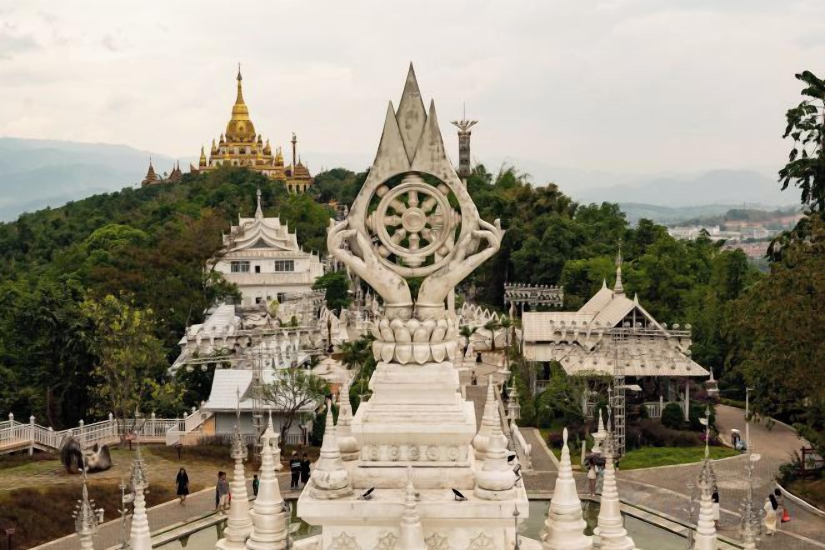 A temple complex with multiple structures, including a prominent white stupa and a golden pagoda in the background.