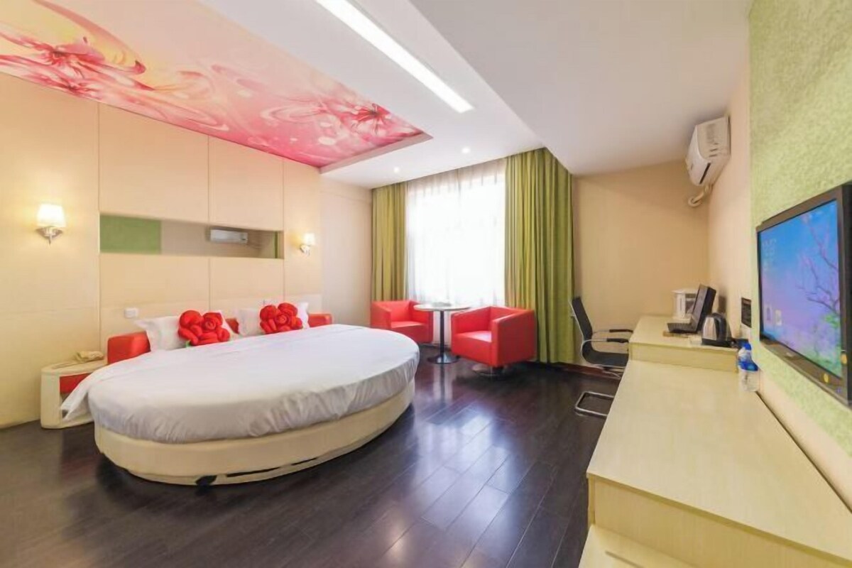 A hotel room with a large bed, a desk, a chair, and a TV.