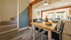 A dining area with a wooden table, black chairs, and a staircase with blue walls. - Jasmine Cottage, Sedgeford, Norfolk (Sedgeford)