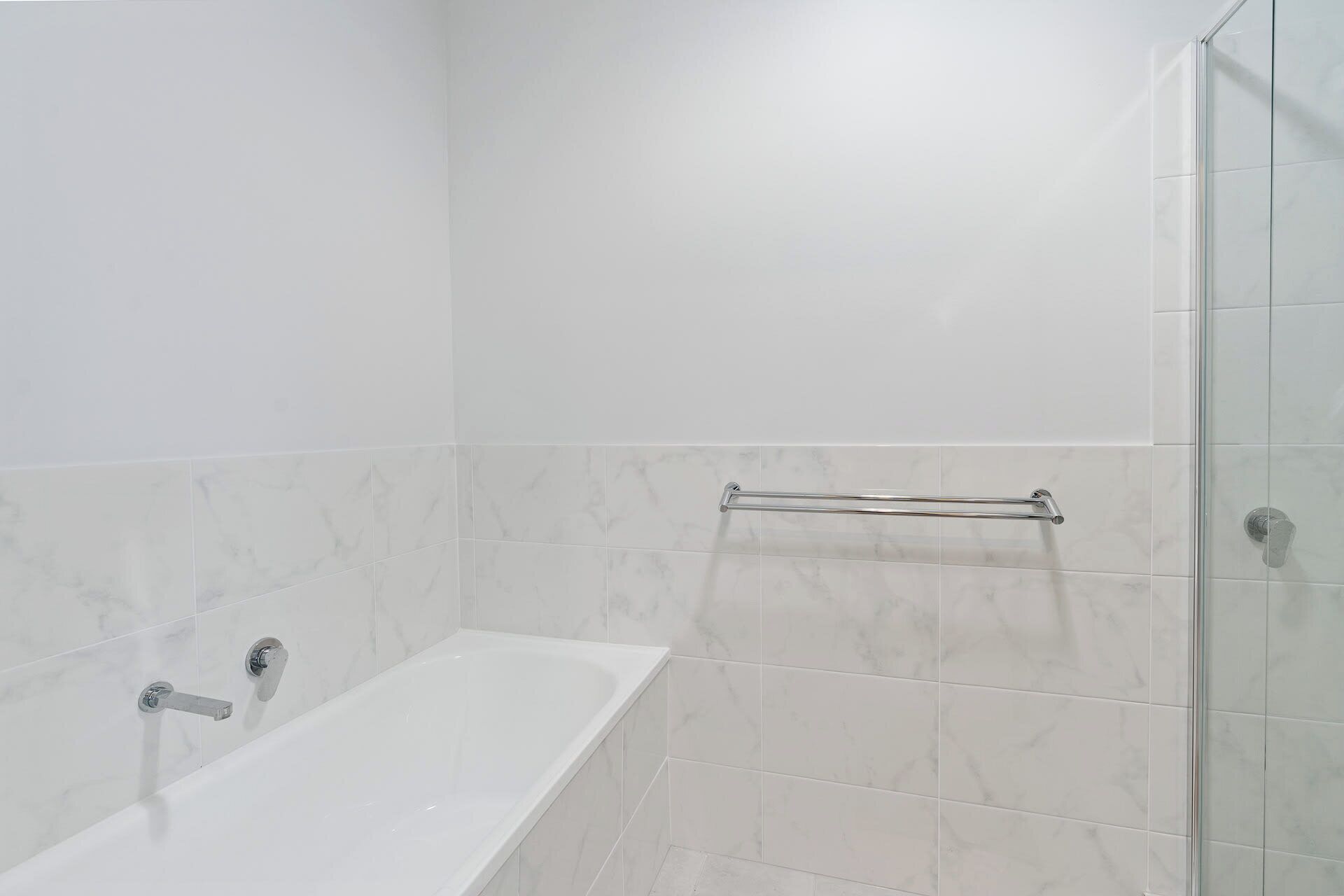 A bathroom with a bathtub, a glass shower enclosure, and a towel rack.