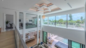 A modern interior with a dining area, kitchen, and a balcony with a view of the outdoors. - Free Golf Cart Aug & Sep! Waterfront Mansion (Naples)