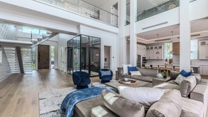 A spacious living area with a high ceiling, a staircase, and a kitchen in the background. - Free Golf Cart Aug & Sep! Waterfront Mansion (Naples)