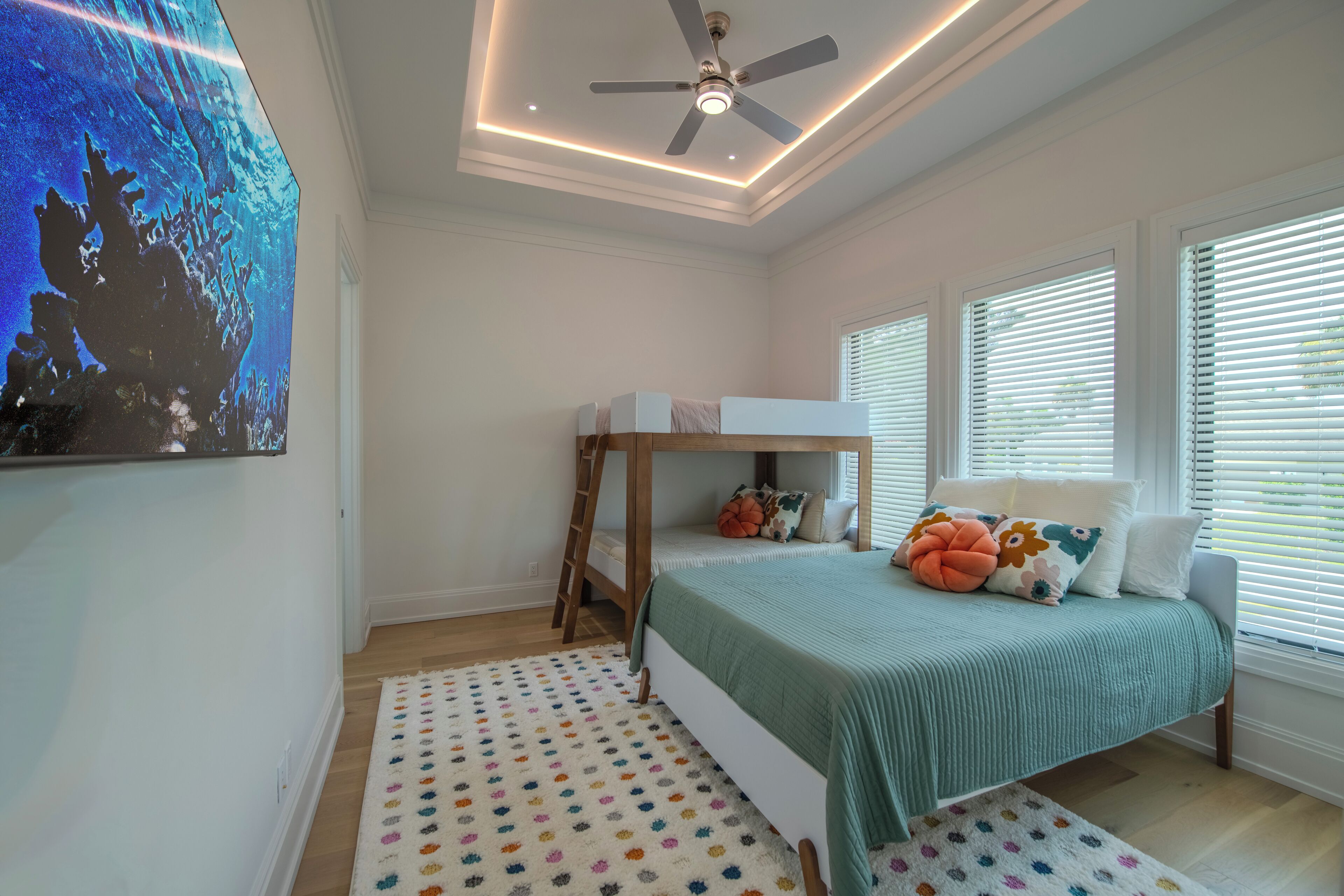 A bedroom with a bunk bed, a ceiling fan, a large painting, and a window with blinds.
