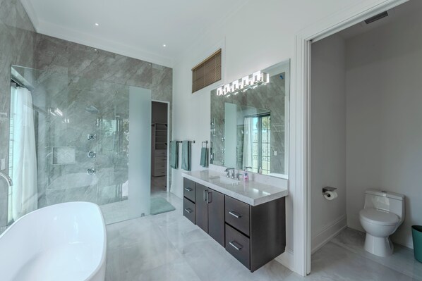 A modern bathroom with a freestanding bathtub, a large vanity with a mirror, a shower enclosure, and a toilet.