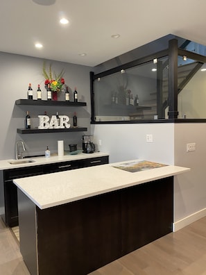 Cozinha moderna com área de bar, com bancada, pia e garrafas de vinho em prateleiras.